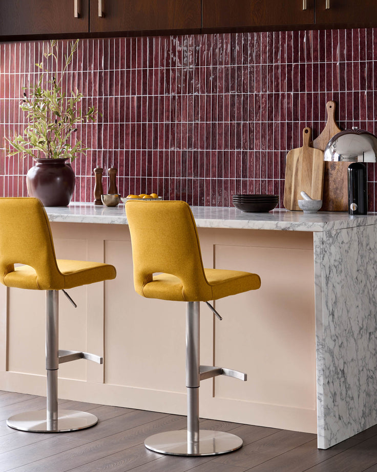 Mustard yellow upholstered gas lift bar stool with curved backrest and brushed metal base, shown at kitchen island.