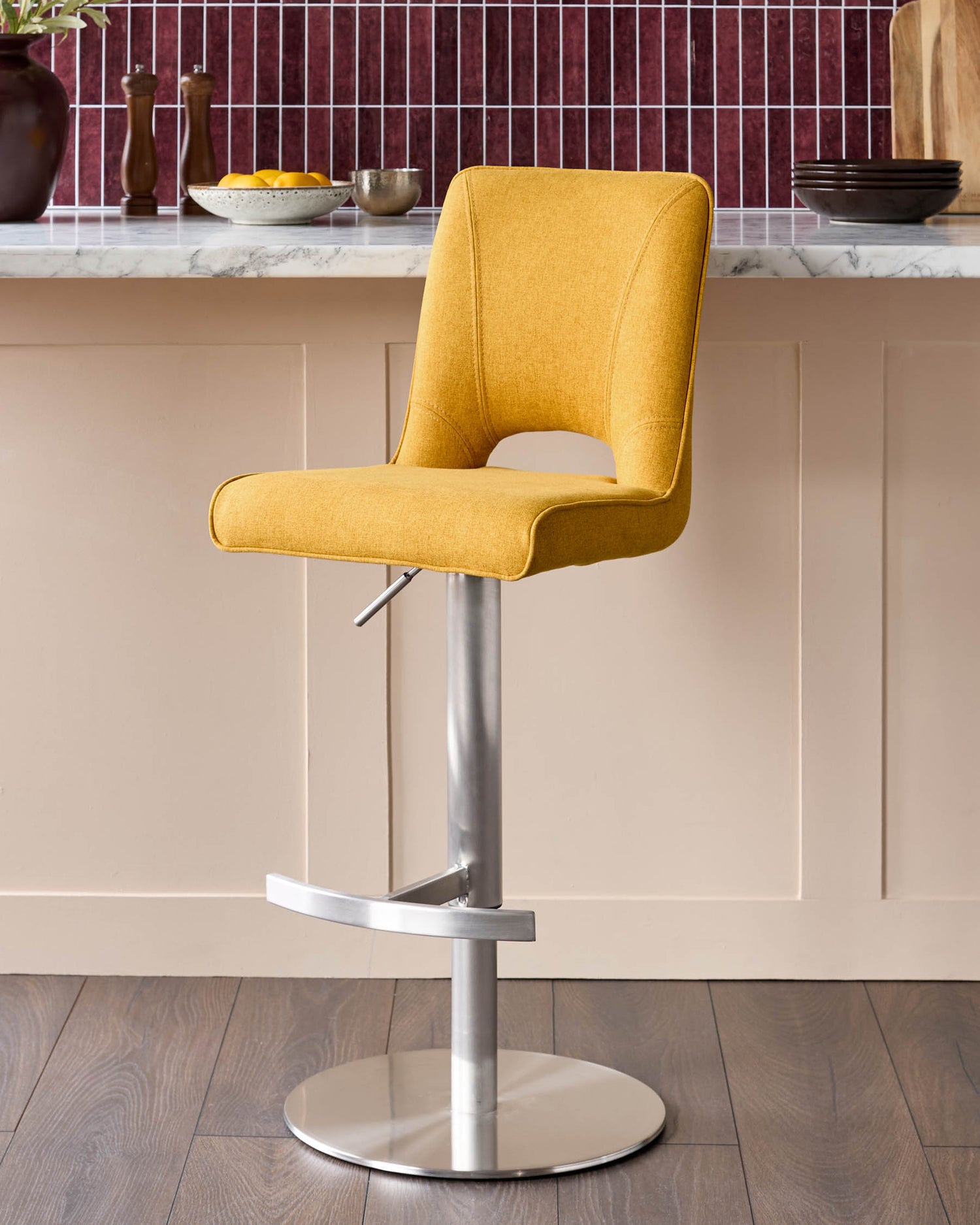 Mustard yellow fabric gas-lift bar stool with curved backrest and brushed metal base, shown at kitchen counter.