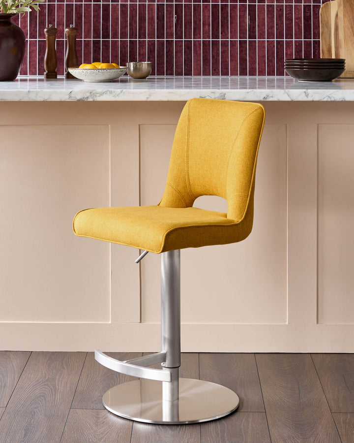 Mustard yellow fabric gas-lift bar stool with brushed metal base and footrest, shown in modern kitchen setting.