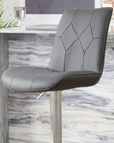 Dark grey quilted bar stool with stainless steel gas lift base, shown at an angle in a modern dining setting.