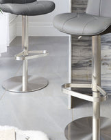 Lumos stainless steel gas lift bar stools with dark grey padded seats, shown in a modern kitchen setting with metallic bases.