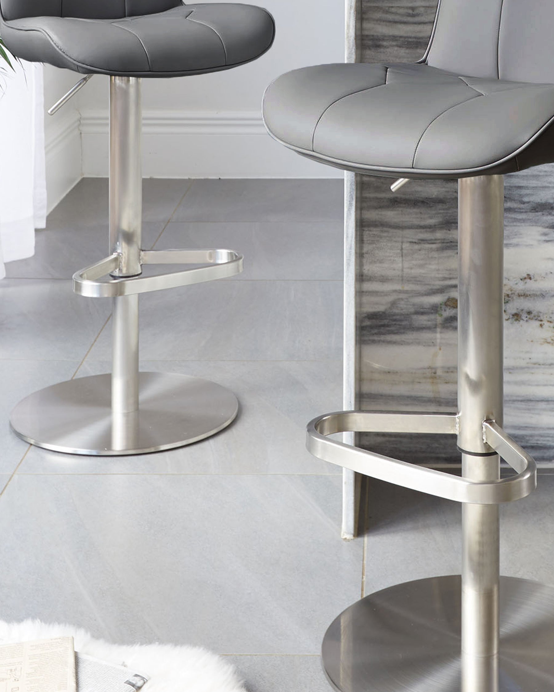 Lumos stainless steel gas lift bar stools with dark grey padded seats, shown in a modern kitchen setting with metallic bases.