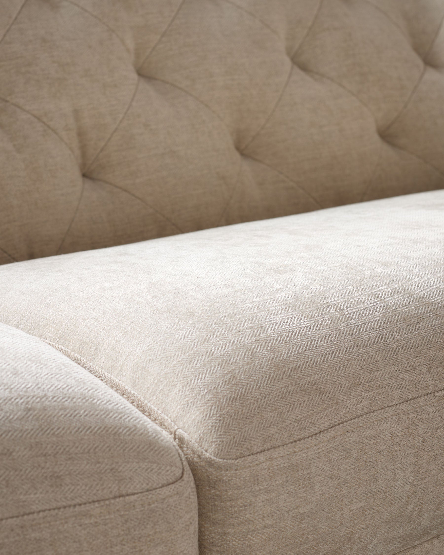 Close-up of a cream-coloured couch featuring button-tufted details and herringbone fabric.