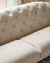 Close-up of a beige, button-backed sofa, showing the textured fabric and plush cushioning.