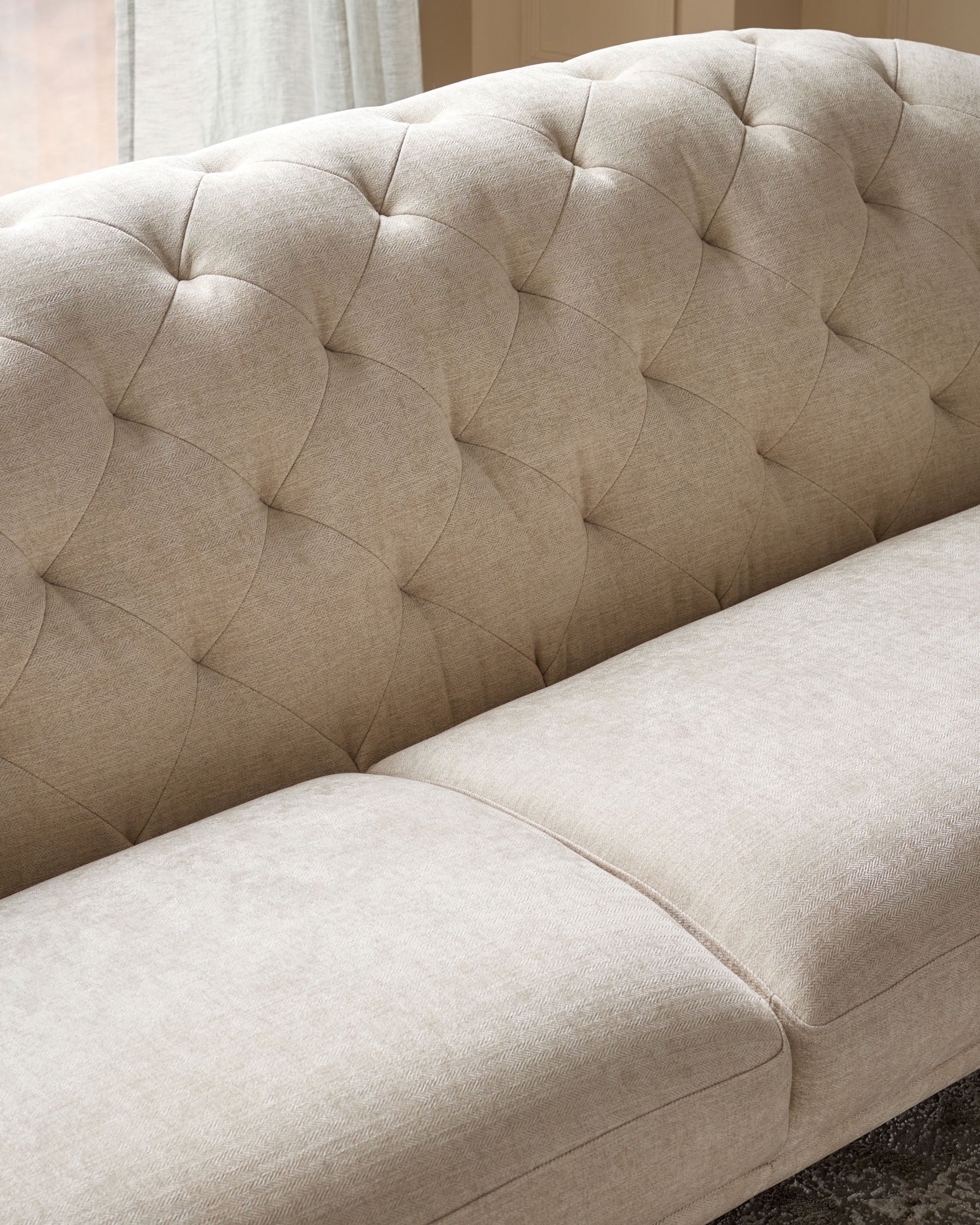 Close-up of a beige, button-backed sofa, showing the textured fabric and plush cushioning.