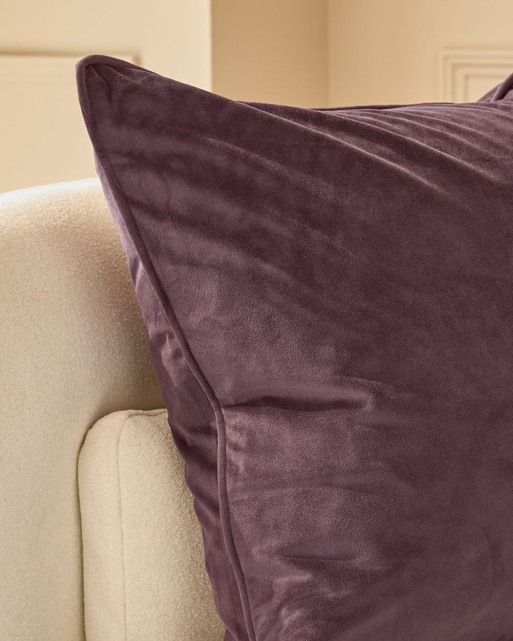 Luca cushion in mulberry velvet, medium size, displayed on a cream upholstered chair arm.