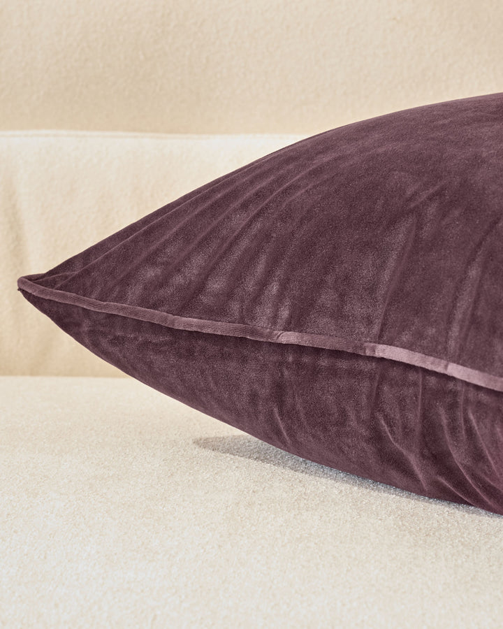 Luca cushion in mulberry, medium size, shown at an angle displaying its plump form and piped seams against a neutral background.