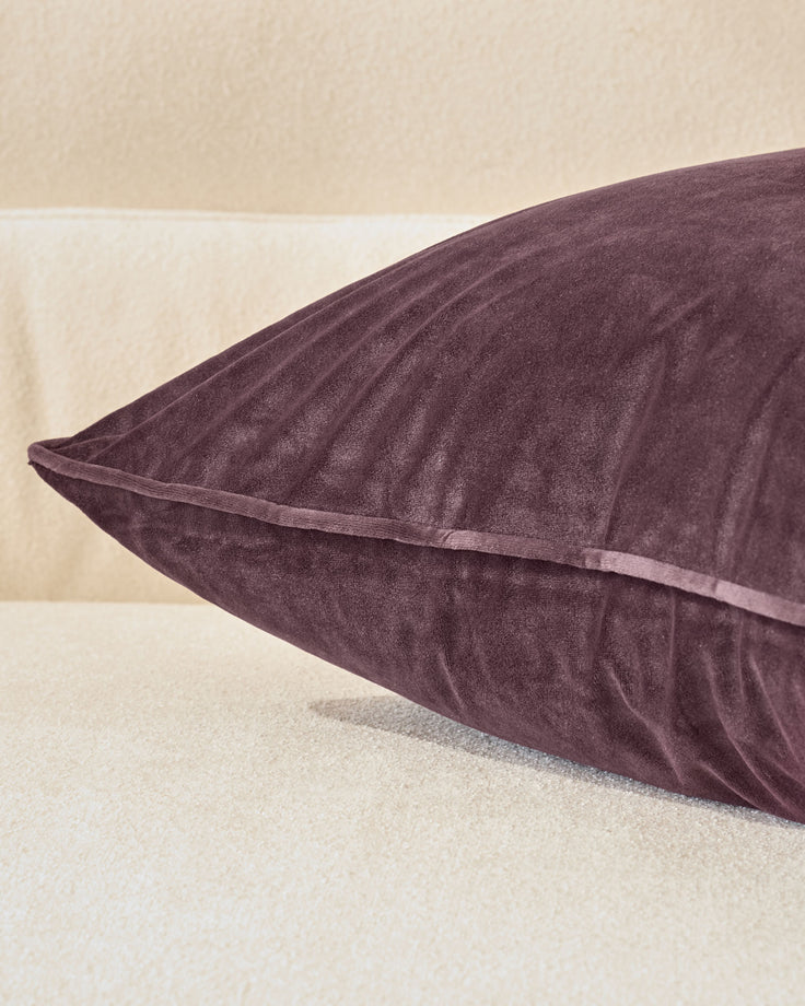Luca cushion in mulberry, medium size, shown at an angle displaying its plump form and piped seams against a neutral background.