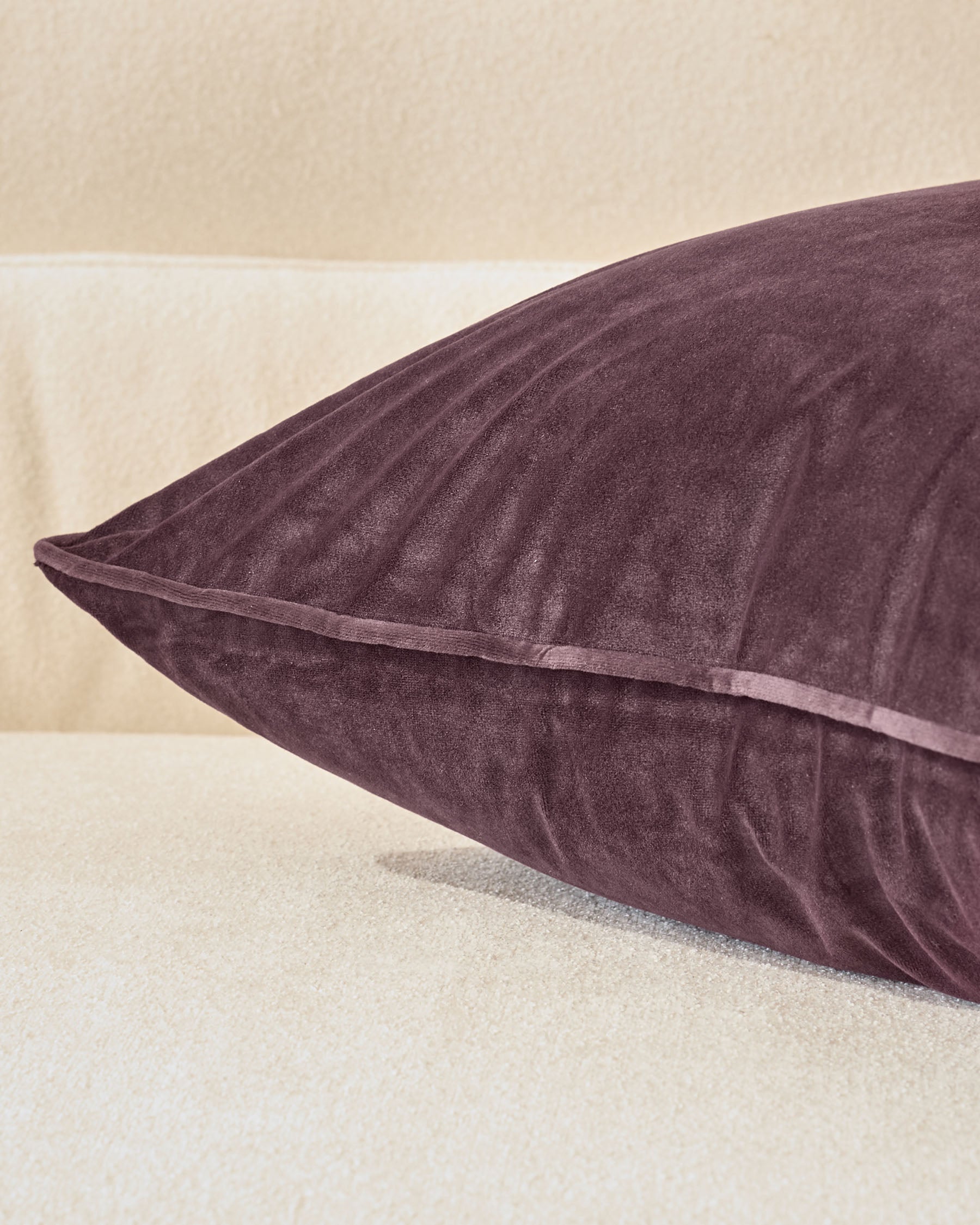 Luca cushion in mulberry, large size, displayed at an angle showing its plump form and piped seam detail against a neutral background.