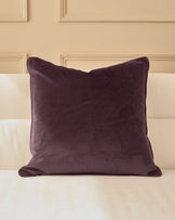 Luca cushion in large mulberry, displayed on a cream upholstered headboard against a paneled wall.