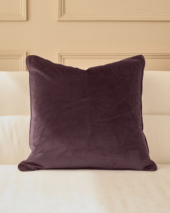 Luca cushion in large mulberry, displayed on a cream upholstered headboard against a paneled wall.