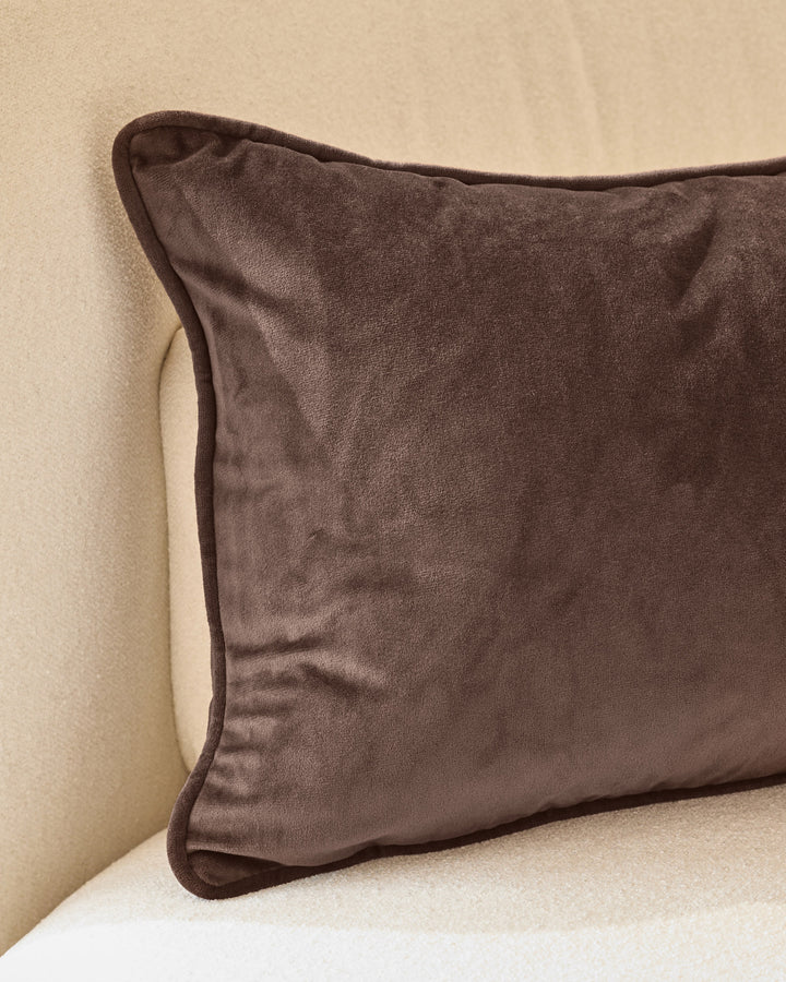 Luca rectangle cushion in chocolate brown velvet with piped edges, displayed on a cream background.