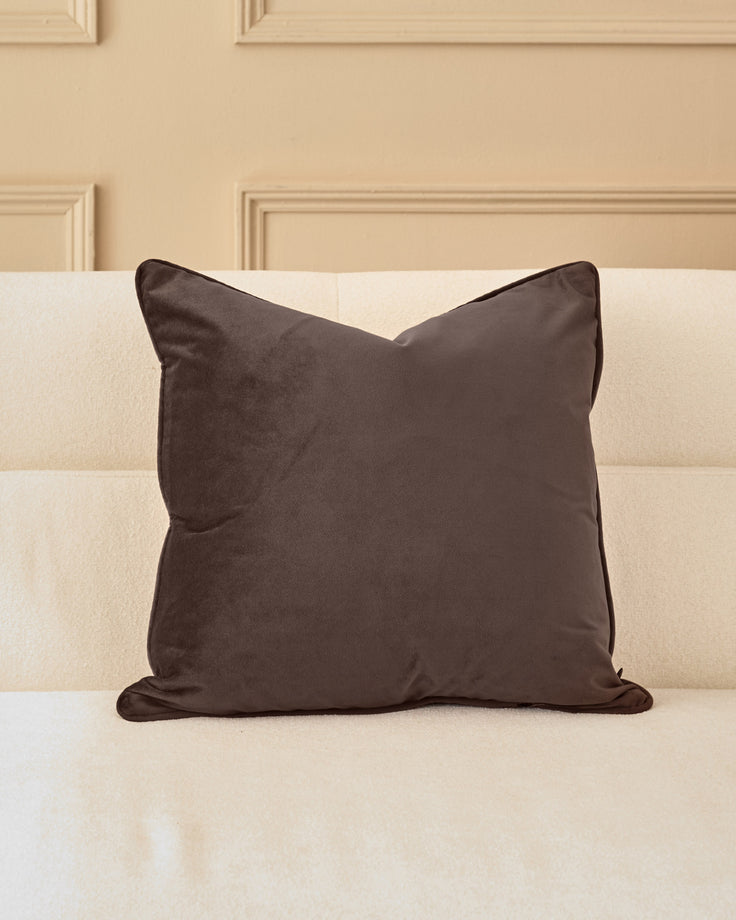 Luca medium chocolate cushion displayed on a cream striped sofa against a beige paneled wall.