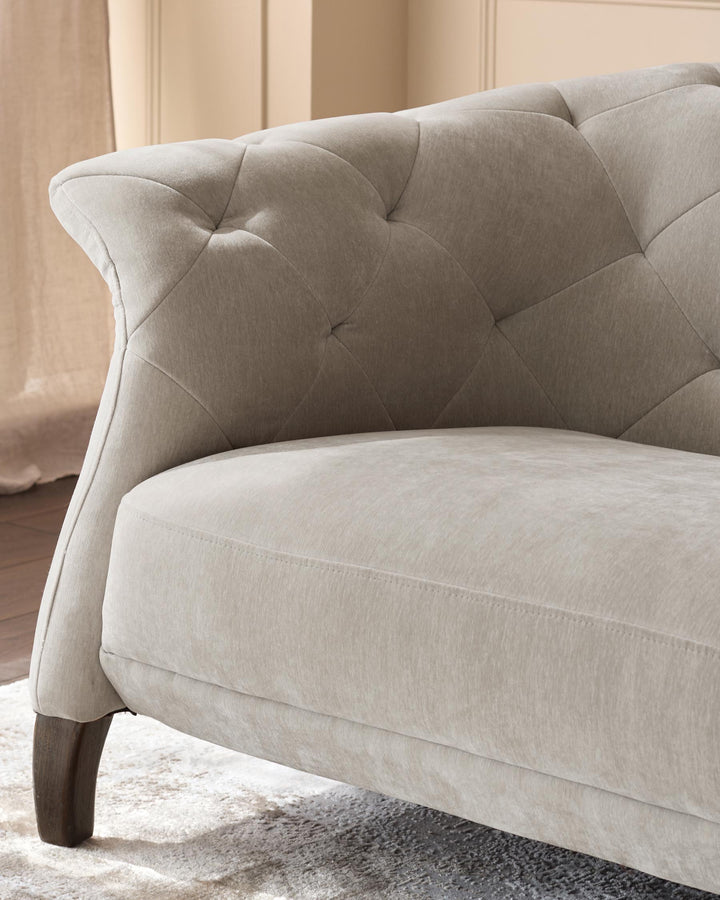 Beige upholstered sofa with button detailing and a curved arm. Shown in a close up, angled view.