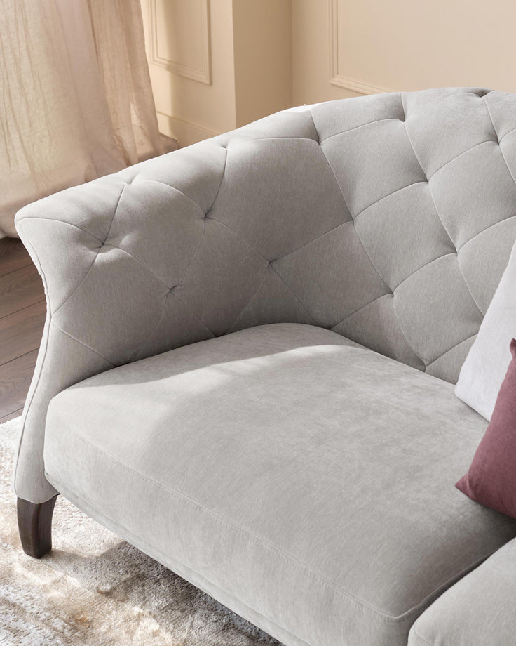 A luxurious, grey, tufted sofa with dark wooden legs, part of a stylish living room set.