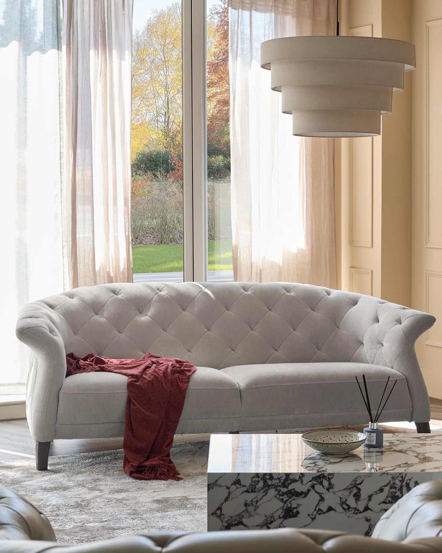Stylish living room featuring a grey Chesterfield sofa, marble-top coffee table, and layered ceiling light fixture.