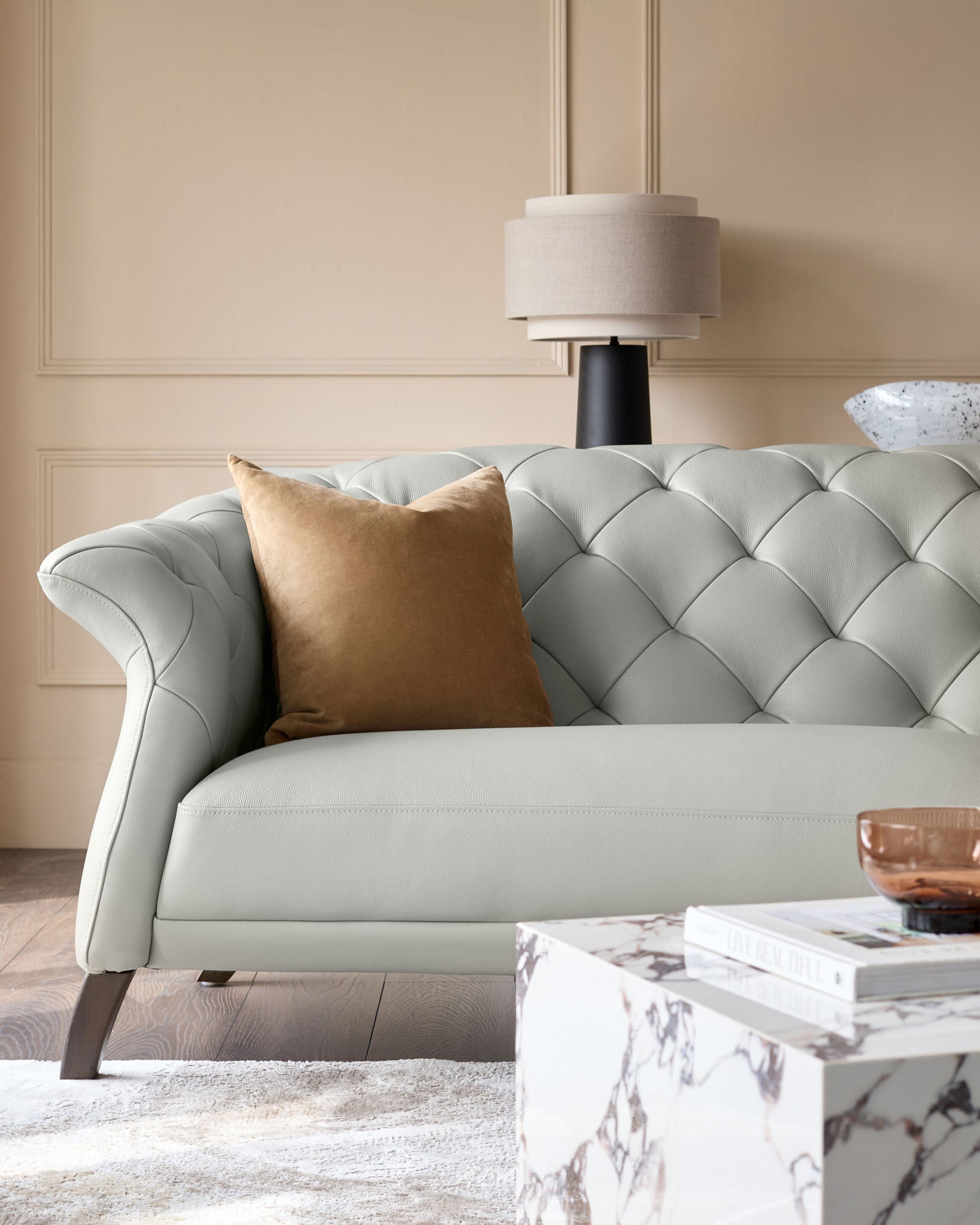 Stylish light grey tufted sofa with tan cushion and a marble effect side table, creating an elegant living space.