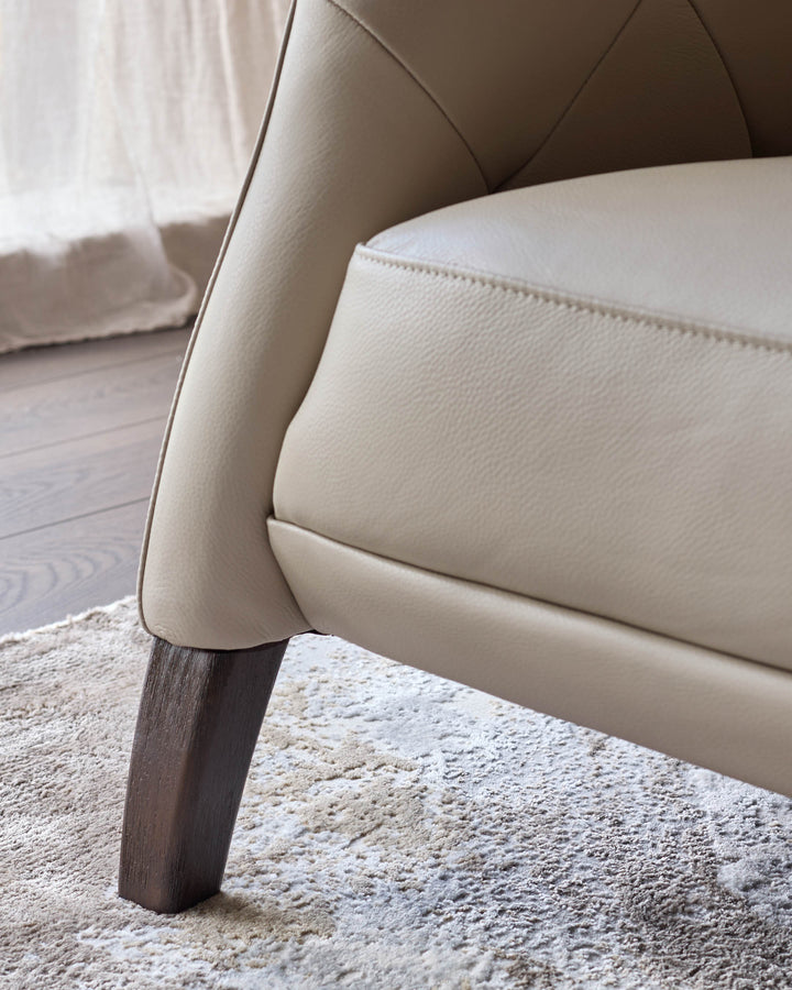 Close-up of a cream leather chair with dark wooden legs, resting on a patterned rug.