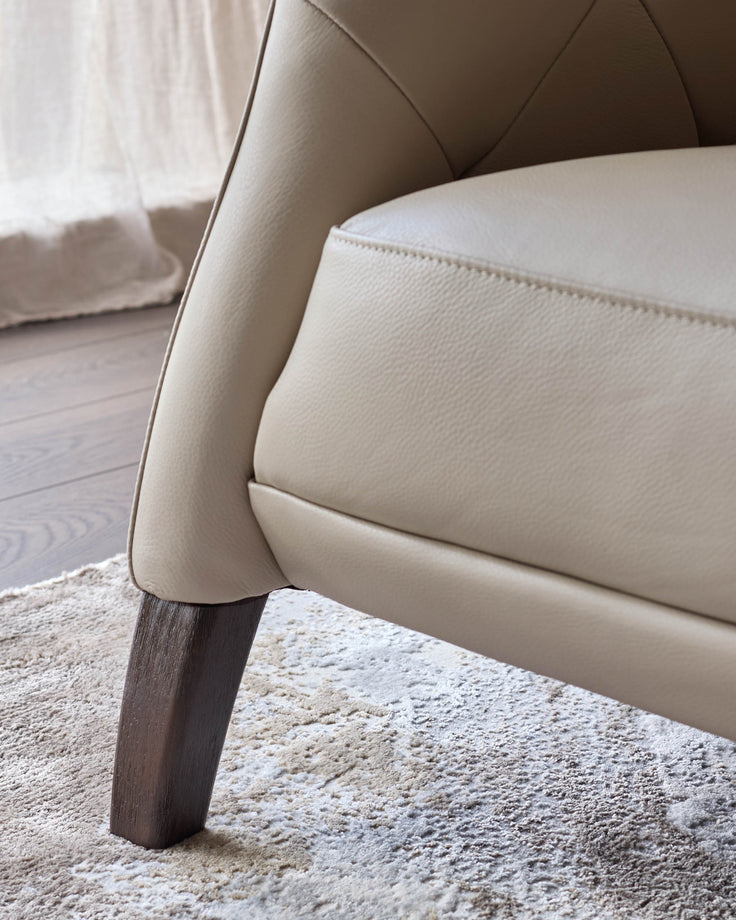Close-up of a cream leather chair with dark wooden legs, resting on a patterned rug.