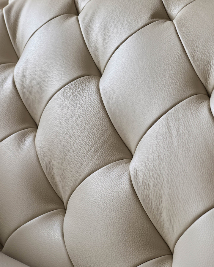 Close-up of a luxurious, cream leather sofa with deep buttoned detailing. Perfect for adding a touch of elegance to your living room.