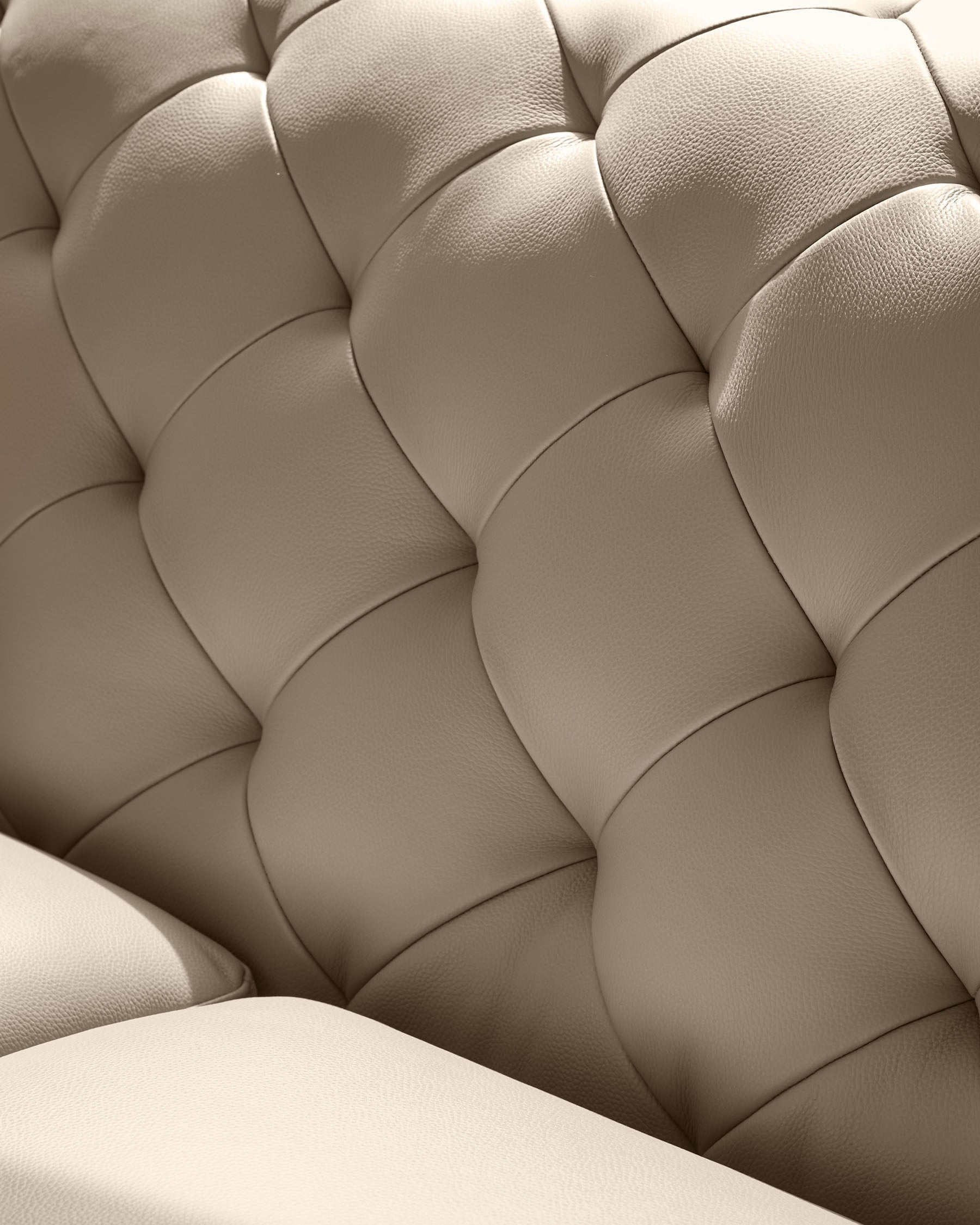 Close-up of a luxurious, button-tufted cream leather sofa, showcasing its texture and design.