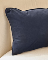 Navy rectangular cushion with piping detail, displayed on a cream-colored upholstered surface against a beige wall.
