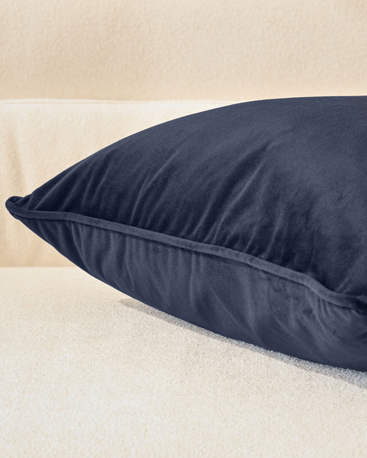 Navy blue rectangular cushion with gathered sides, displayed on sand-colored surface against beige background.
