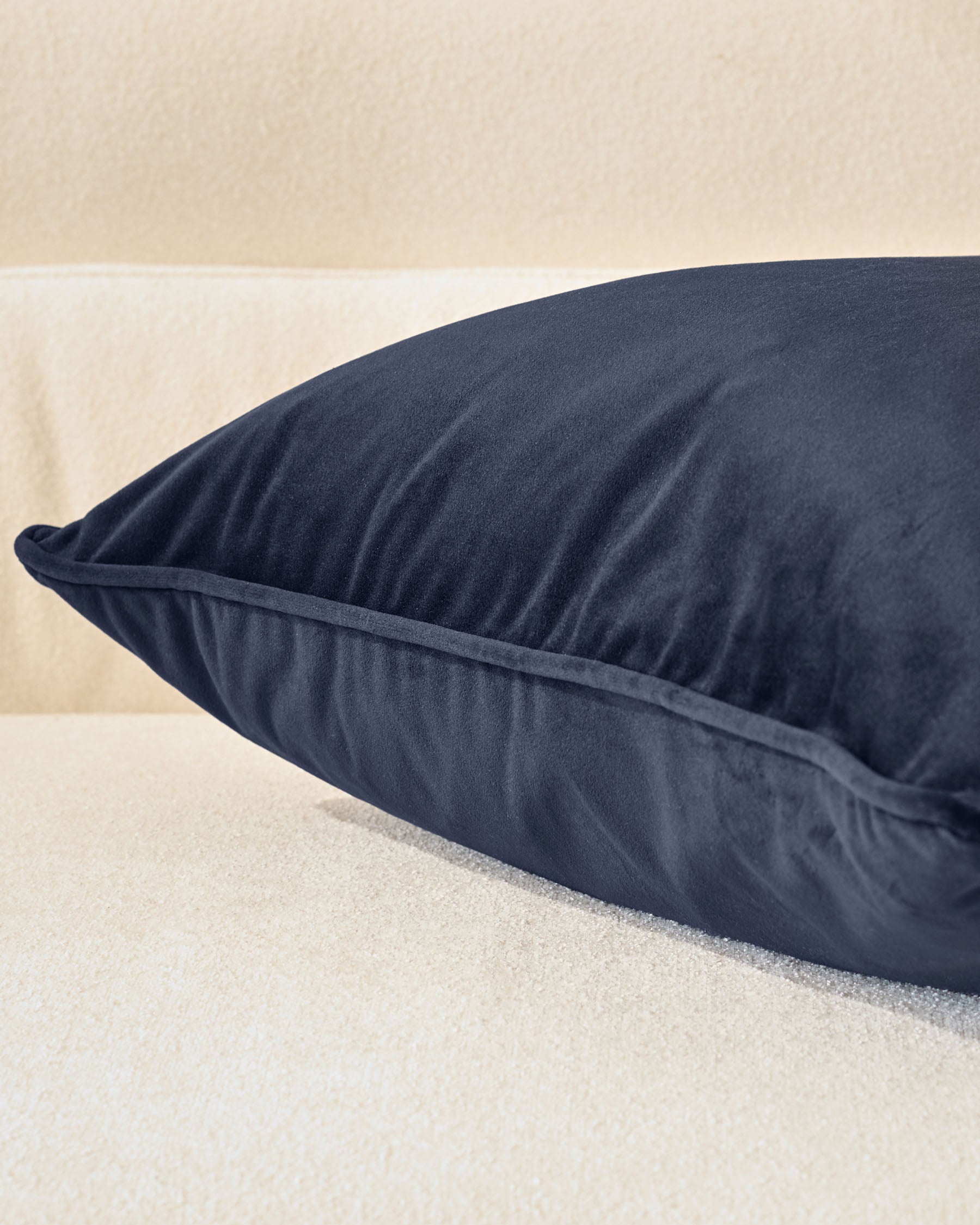 Navy rectangular cushion with visible seam detail, positioned on light sand-colored surface against neutral background.