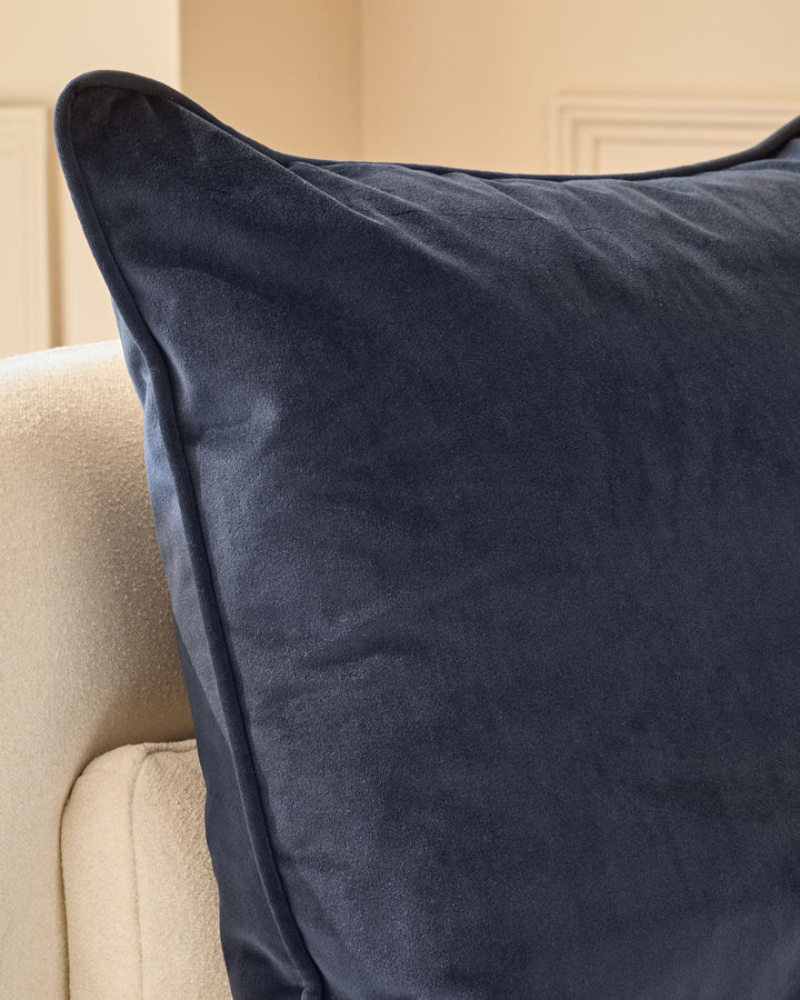 Navy velvet cushion with piping detail, displayed on a cream upholstered chair back.