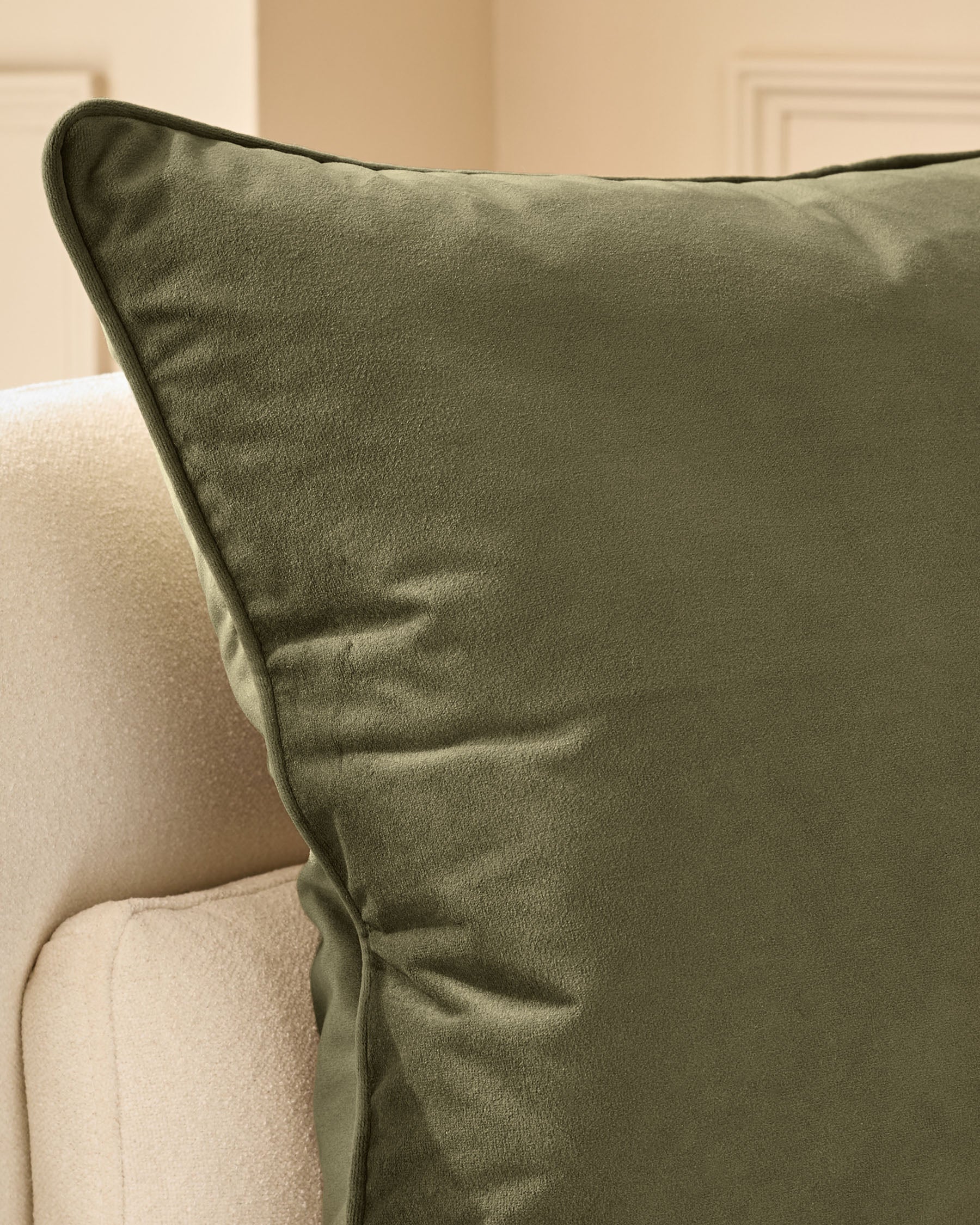 Luca medium cushion in olive green with dark piping, displayed on a cream upholstered chair.