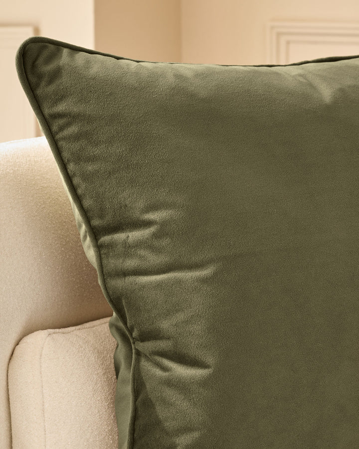 Luca medium cushion in olive green with dark piping, displayed on a cream upholstered chair.