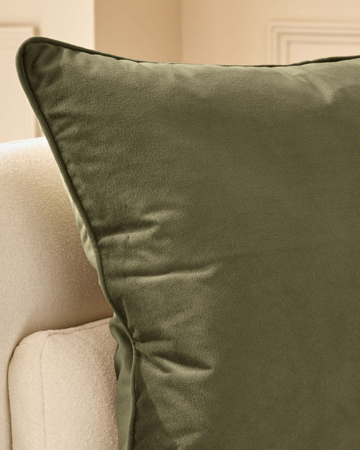 Luca medium cushion in olive green with dark piping, displayed on a cream upholstered chair.