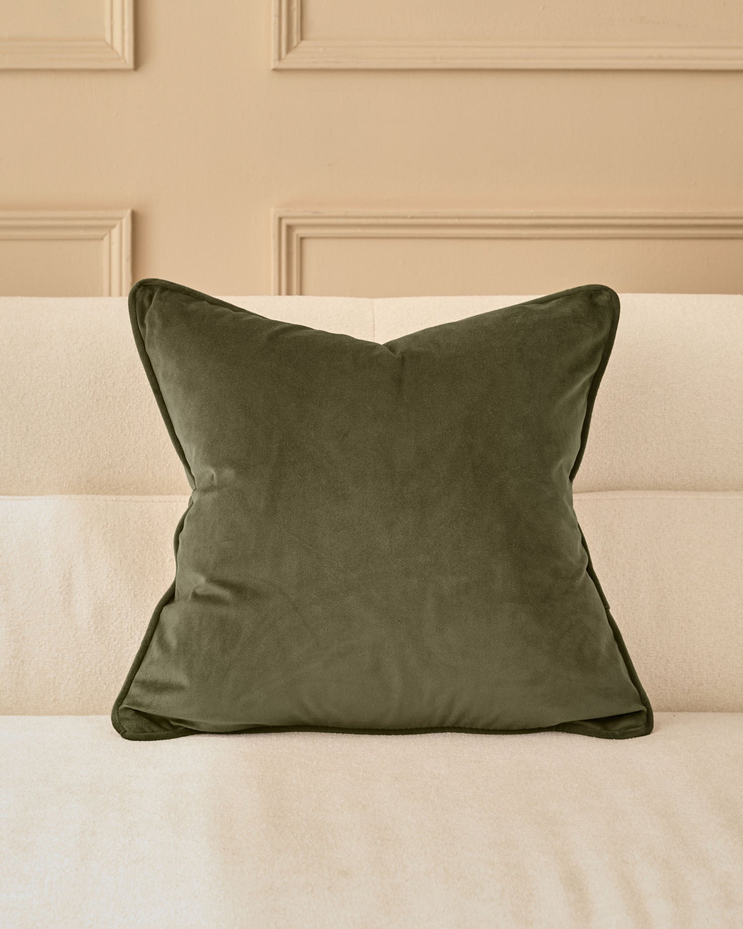 Luca Cushion in Medium Olive Green displayed on a cream striped sofa against a beige paneled wall.