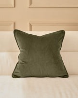 Luca Cushion in Medium Olive Green displayed on a cream striped sofa against a beige paneled wall.