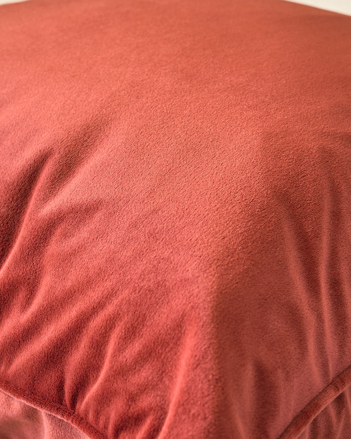Large Luca cushion in toffee red with soft, textured fabric and subtle gathering detail visible on the surface.
