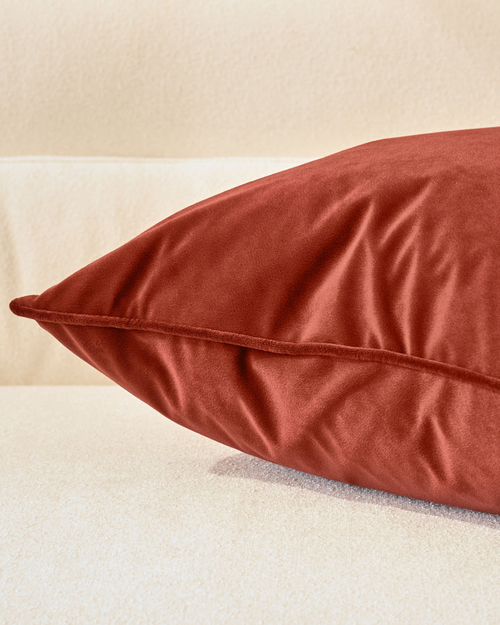 Luca rectangle cushion in toffee red velvet, displayed at an angle showing its piped seam detail and soft texture against a neutral background.