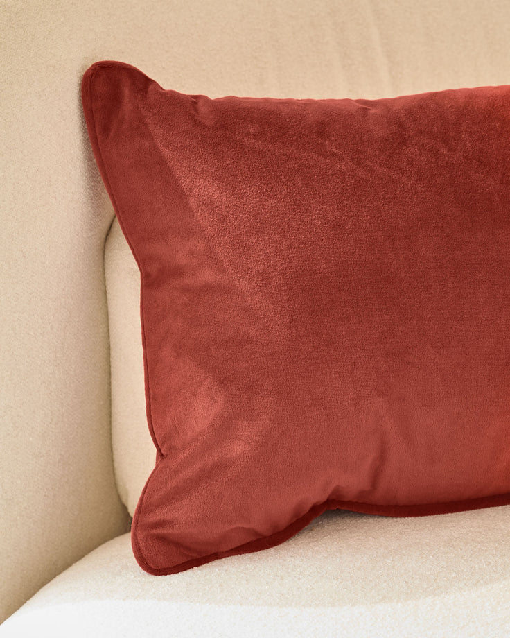 Luca rectangle cushion in toffee red, displayed on a cream sofa against a beige wall.