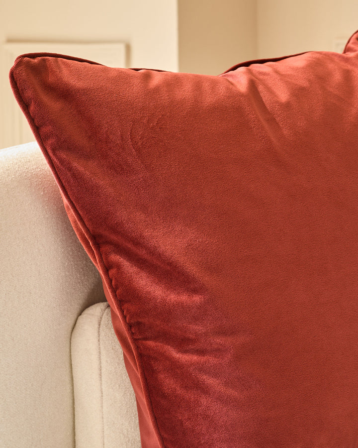 Large toffee red velvet cushion with piping detail, displayed on a cream upholstered armchair.