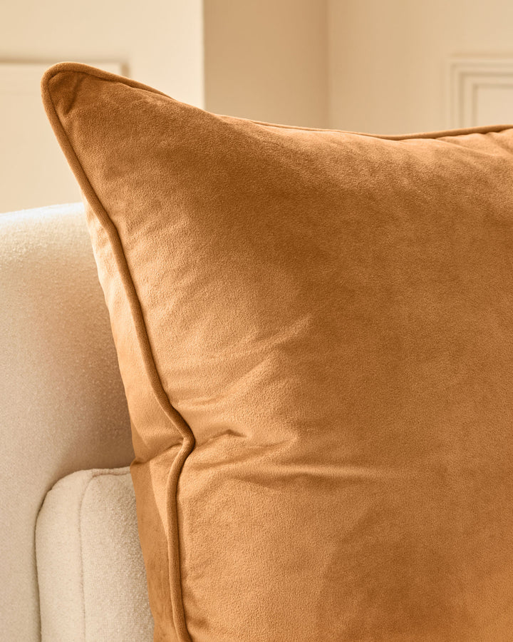 Luca large caramel cushion with piped edges, displayed on a cream upholstered chair.