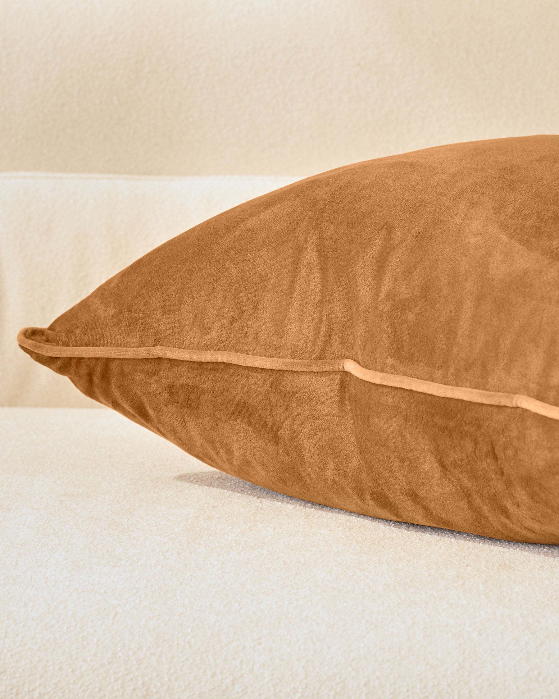 Luca cushion in caramel, large size, shown from side angle on neutral background displaying its plush texture and piping detail.