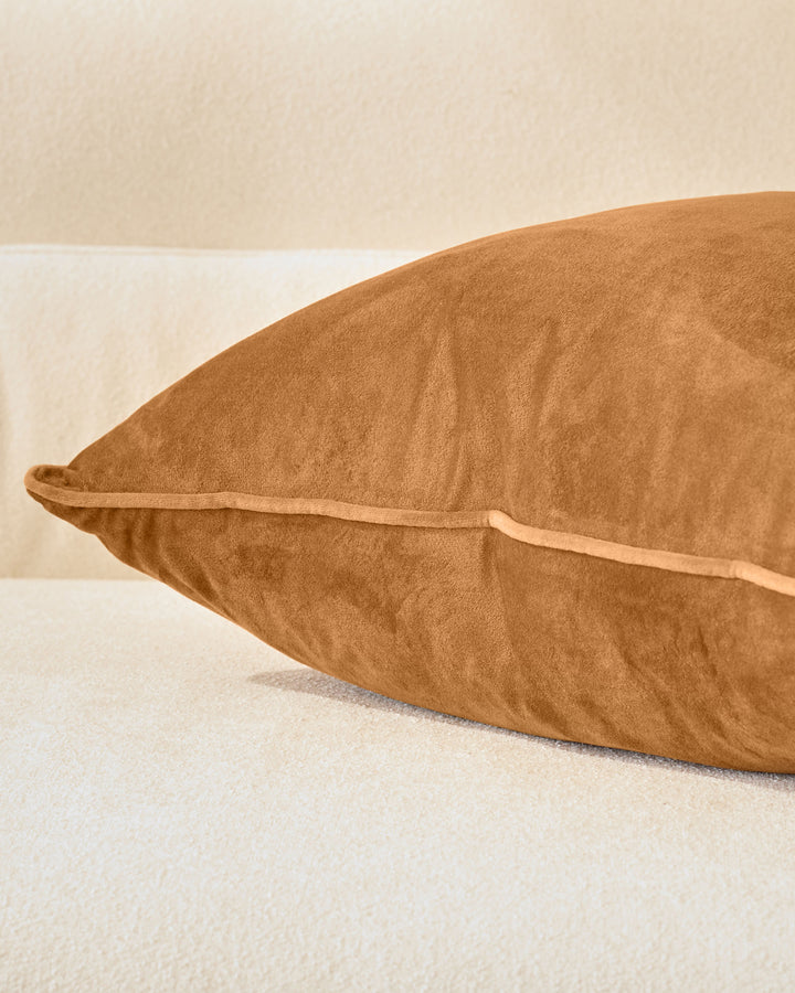 Luca cushion in caramel, large size, shown from side angle on neutral background displaying its plush texture and piping detail.
