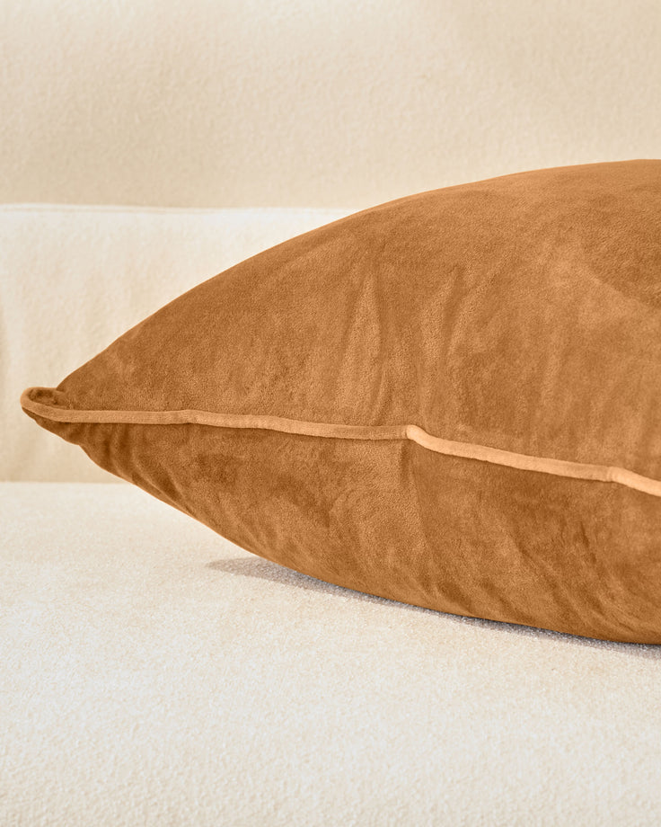 Luca cushion in caramel, large size, shown from side angle on neutral background displaying its plush texture and piping detail.