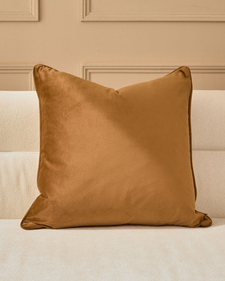 Luca Cushion Large in caramel, displayed on a cream upholstered bed against a neutral wall with paneling.