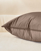 Luca cushion in mink, medium size, displayed at an angle showing its plump profile and piped seam detail against a neutral background.
