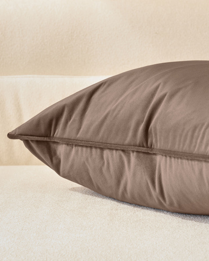 Luca cushion in mink, medium size, displayed at an angle showing its plump profile and piped seam detail against a neutral background.