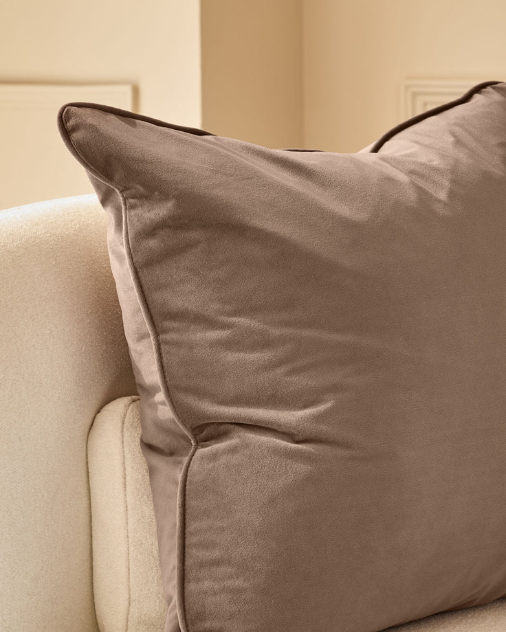 Large mink velvet cushion with piping detail, displayed on a cream upholstered chair.