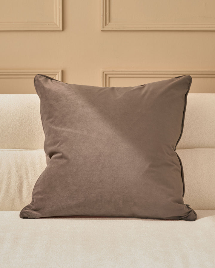 Luca cushion in mink, large square pillow with piped edges on cream upholstered bed.