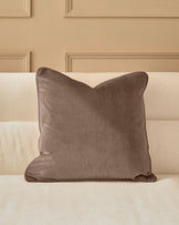 Luca cushion in mink velvet displayed on a cream upholstered headboard against a neutral wall.