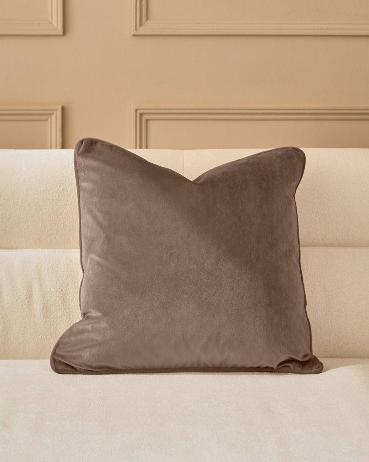 Luca cushion in mink velvet displayed on a cream upholstered headboard against a neutral wall.