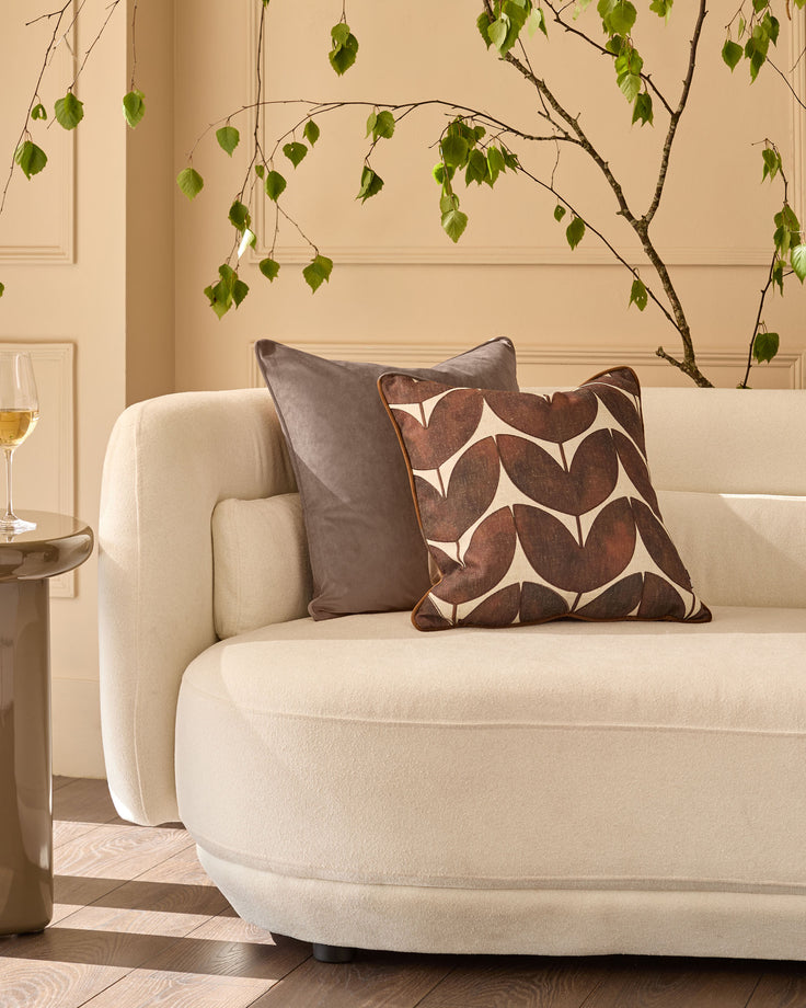 Mink velvet cushion with piping displayed on cream armchair in styled living room setting.
